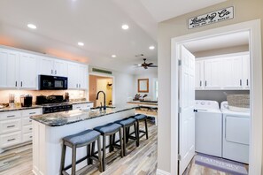 A modern kitchen with white cabinets, a granite countertop, and a built-in island with bar stools. - 'leaping Toad Ranch' ~ 9 Mi to Lake Granbury! (Granbury)