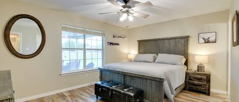 Quarto com uma cama grande, um ventilador de teto, uma janela, um espelho e um banco de madeira.