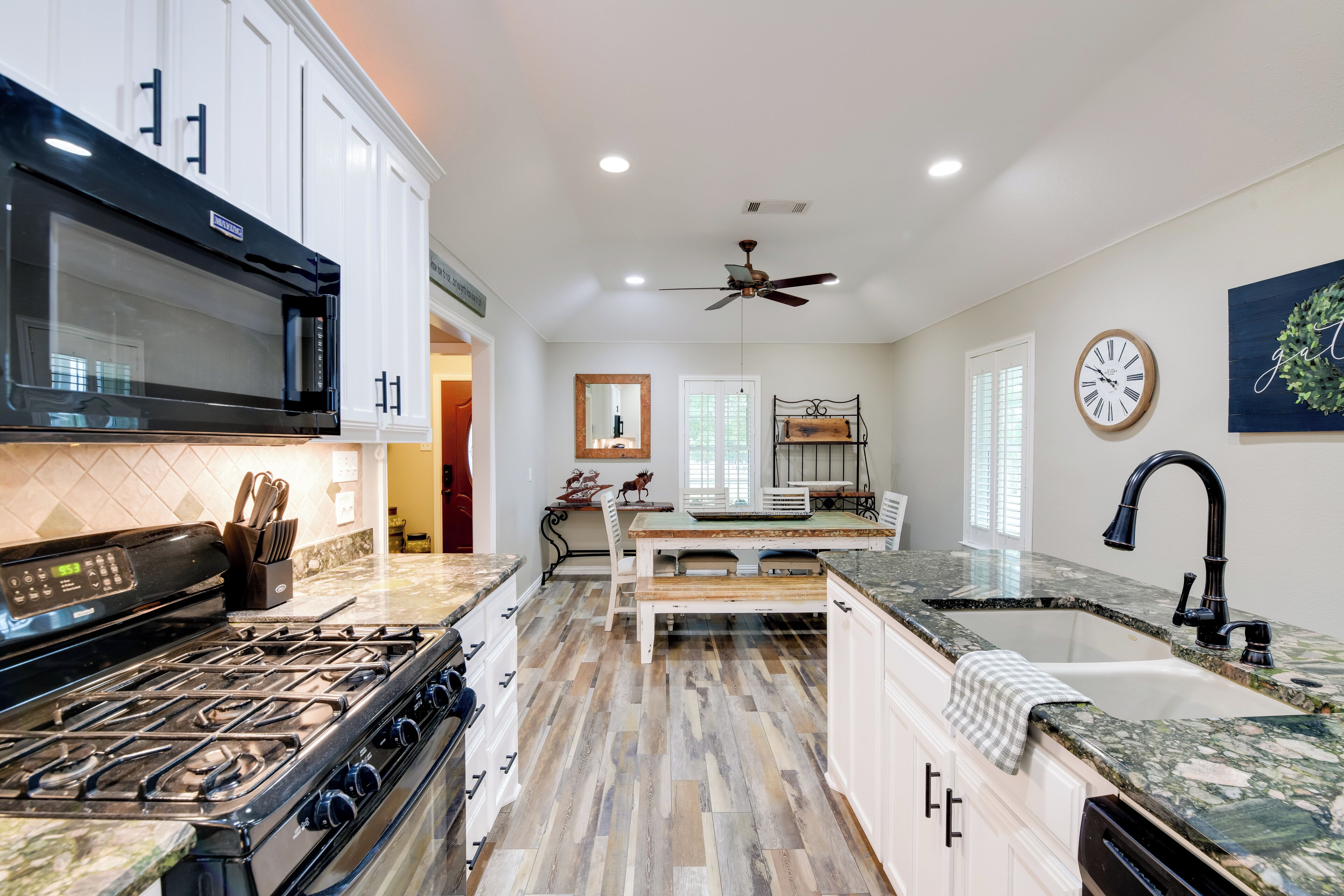 A kitchen with white cabinets, a black stove, a wooden dining table, and a sink.