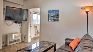 Ein Wohnzimmer mit Flachbildfernseher, Klimaanlage und einem Sofa mit einem orangefarbenen Kissen.
