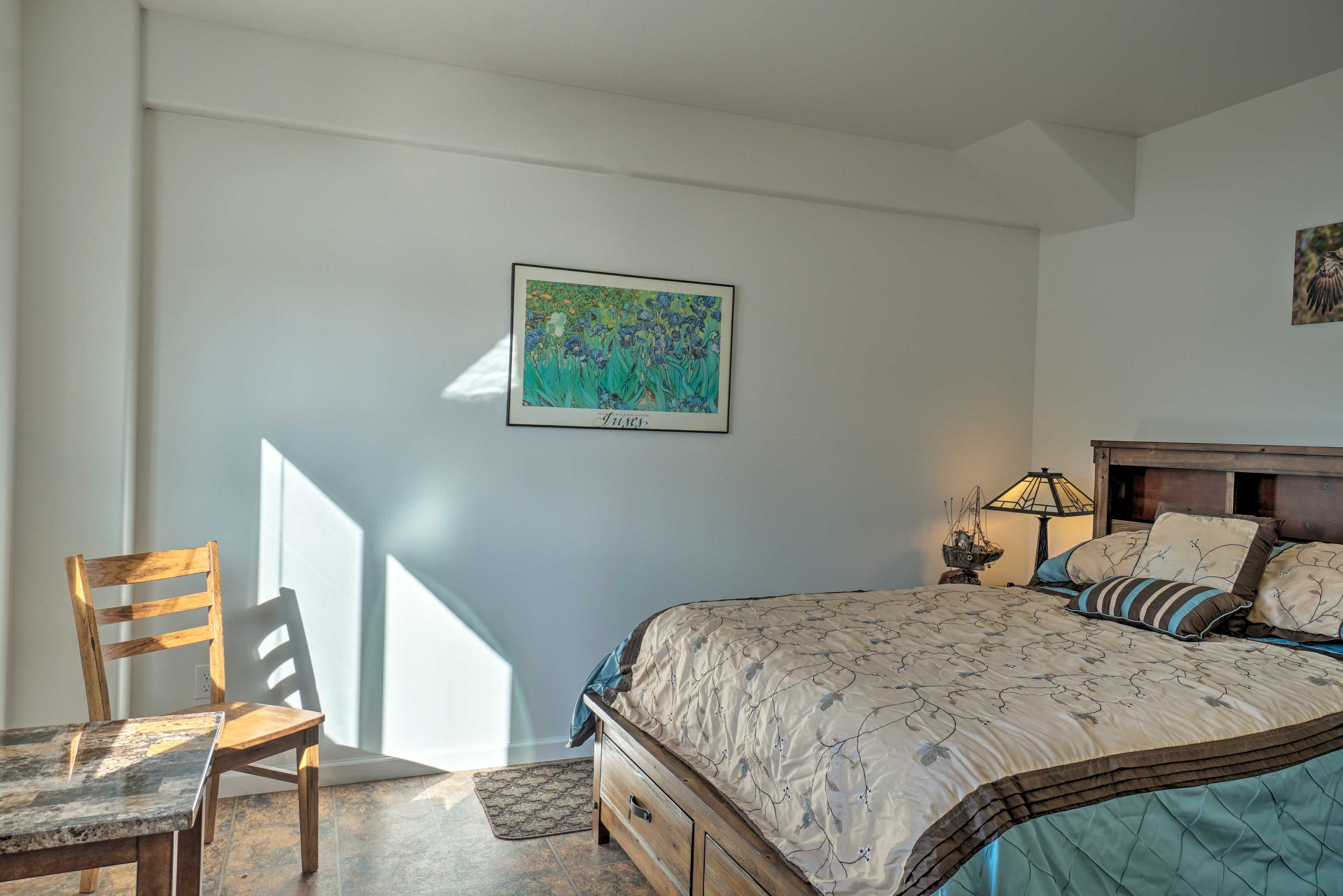 A bedroom with a bed, a chair, a table, and a wall-mounted picture.