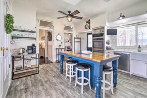 Una cocina con una isla azul, armarios blancos y un ventilador de techo.