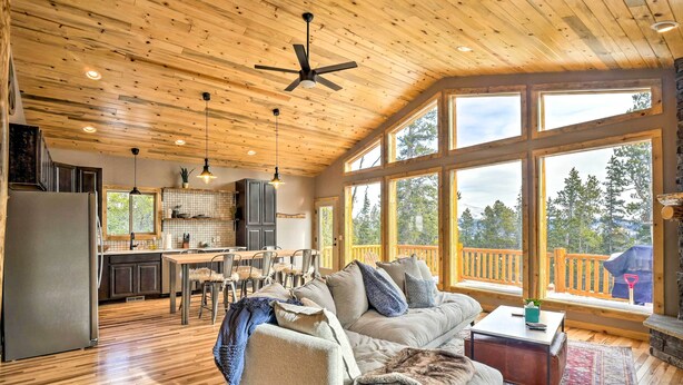 A spacious cabin interior with a kitchen, dining area, and a large window overlooking a deck. - Mountainside Fairplay Cabin w/ Game Room & Sauna! (Fairplay)