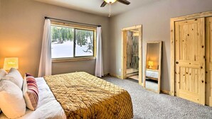 A bedroom with a bed, a ceiling fan, a window with curtains, a mirror, and wooden doors. - Mountainside Fairplay Cabin w/ Game Room & Sauna! (Fairplay)