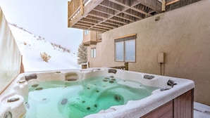 Uma banheira de hidromassagem com deck de madeira e montanhas nevadas ao fundo.