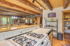 A rustic kitchen with a large island, wooden ceiling beams, and a stove.