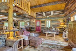 A log cabin interior with a wooden staircase, a red door, and a fireplace.