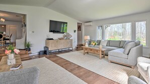 Een ruime woonkamer met een grote modulaire bank, een salontafel en een open haard. Achtergrond toont een eethoek.