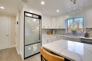 Una cocina moderna con armarios blancos, una isla grande y vistas a árboles por la ventana.
