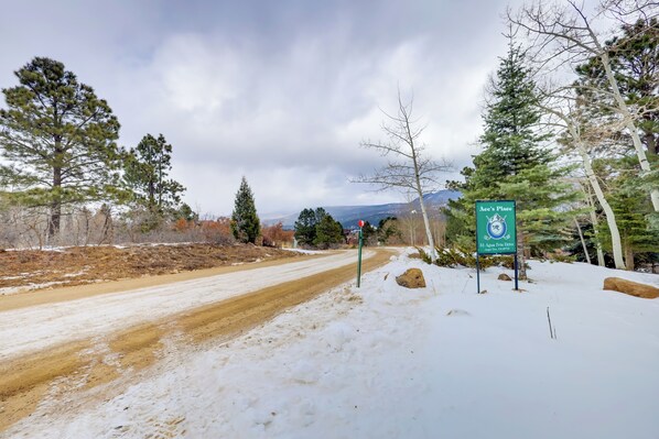 A snow-covered road with a sign for 'Ace's Place' at 31 Agua Fria Drive, indicating a mountain resort.