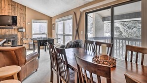 A dining area with a wooden table, chairs, and a candle centerpiece. There is a television mounted on the wall and a fireplace in the background. - 3BR Riverfront Retreat 1 Min to Vail or BC Shuttle (Avon)