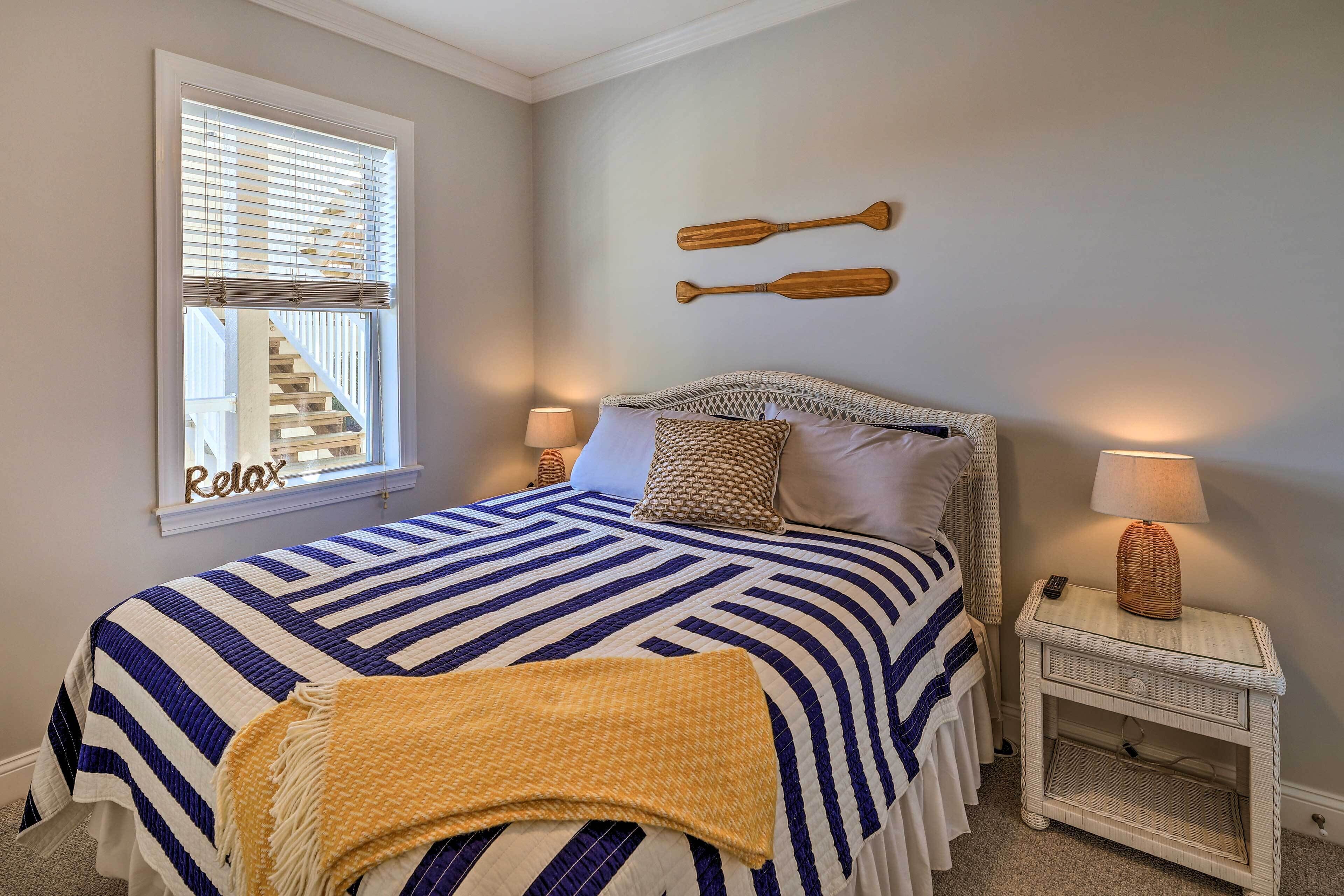 A bedroom with a bed, two wall-mounted paddles, a window with blinds, a bedside table with a lamp, and a 'Relax' sign on the wall.