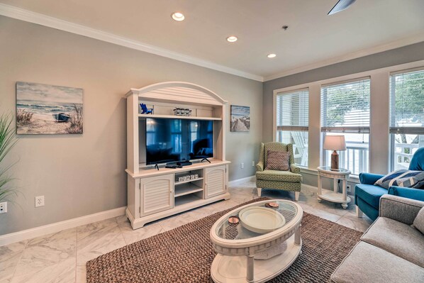 A living room with a TV, a fireplace, a coffee table, and a view of the outdoors. - Ocean Club Condo w/ Community Pool & Hot Tub (Atlantic Beach)