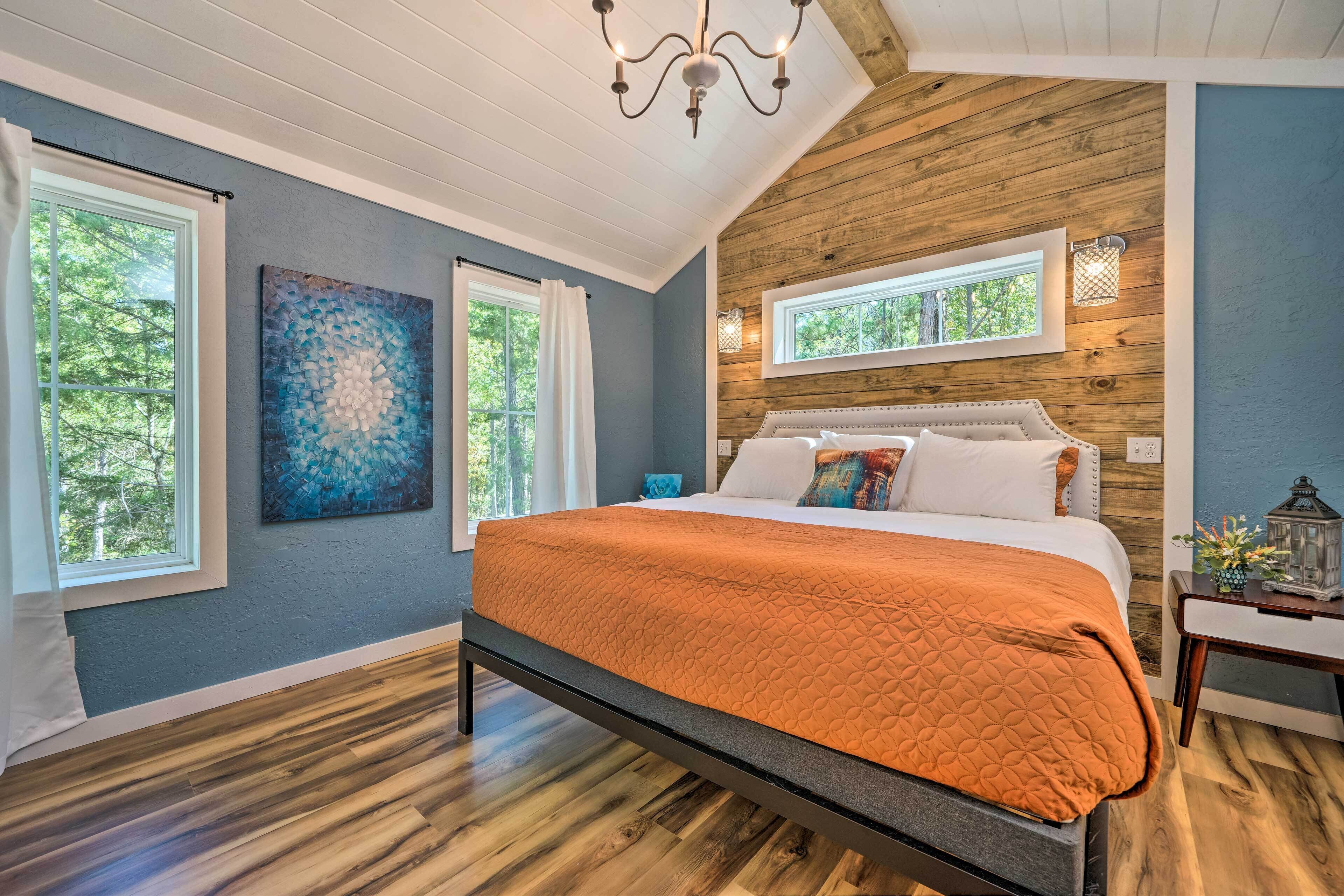 A bedroom with a large bed, wooden ceiling, and two windows.