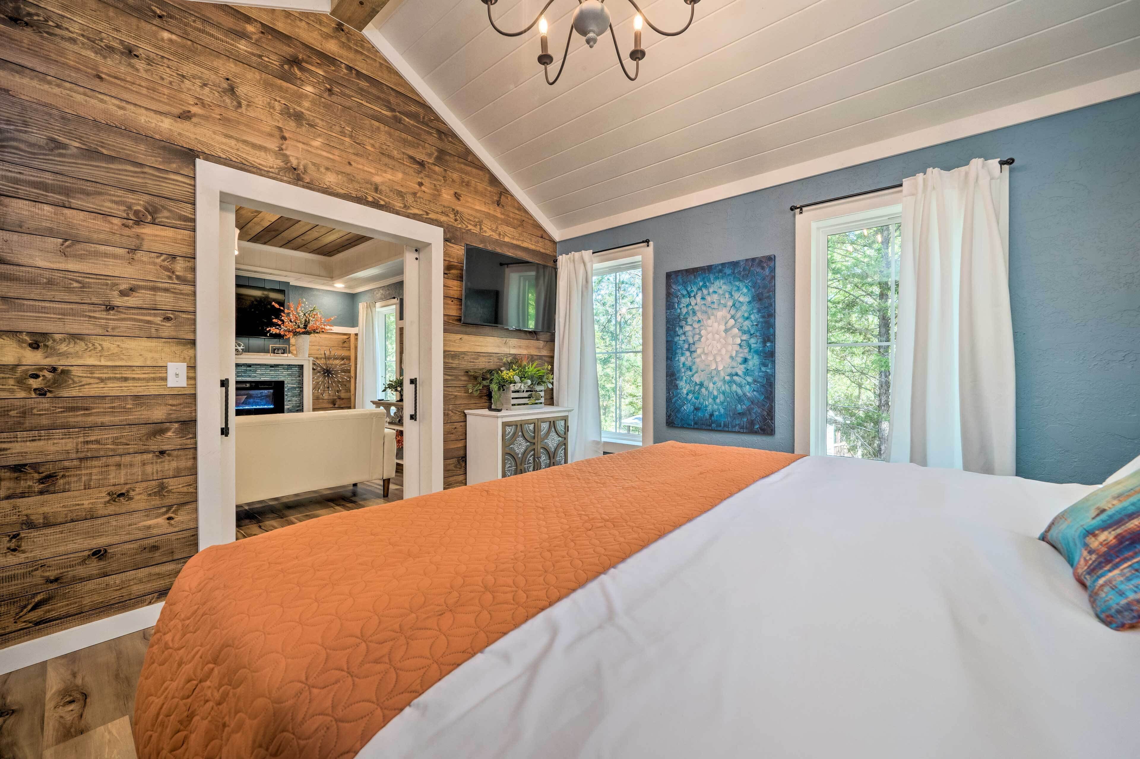 A bedroom with a wooden ceiling, a large bed with an orange bedspread, a white headboard, and a window with white curtains.