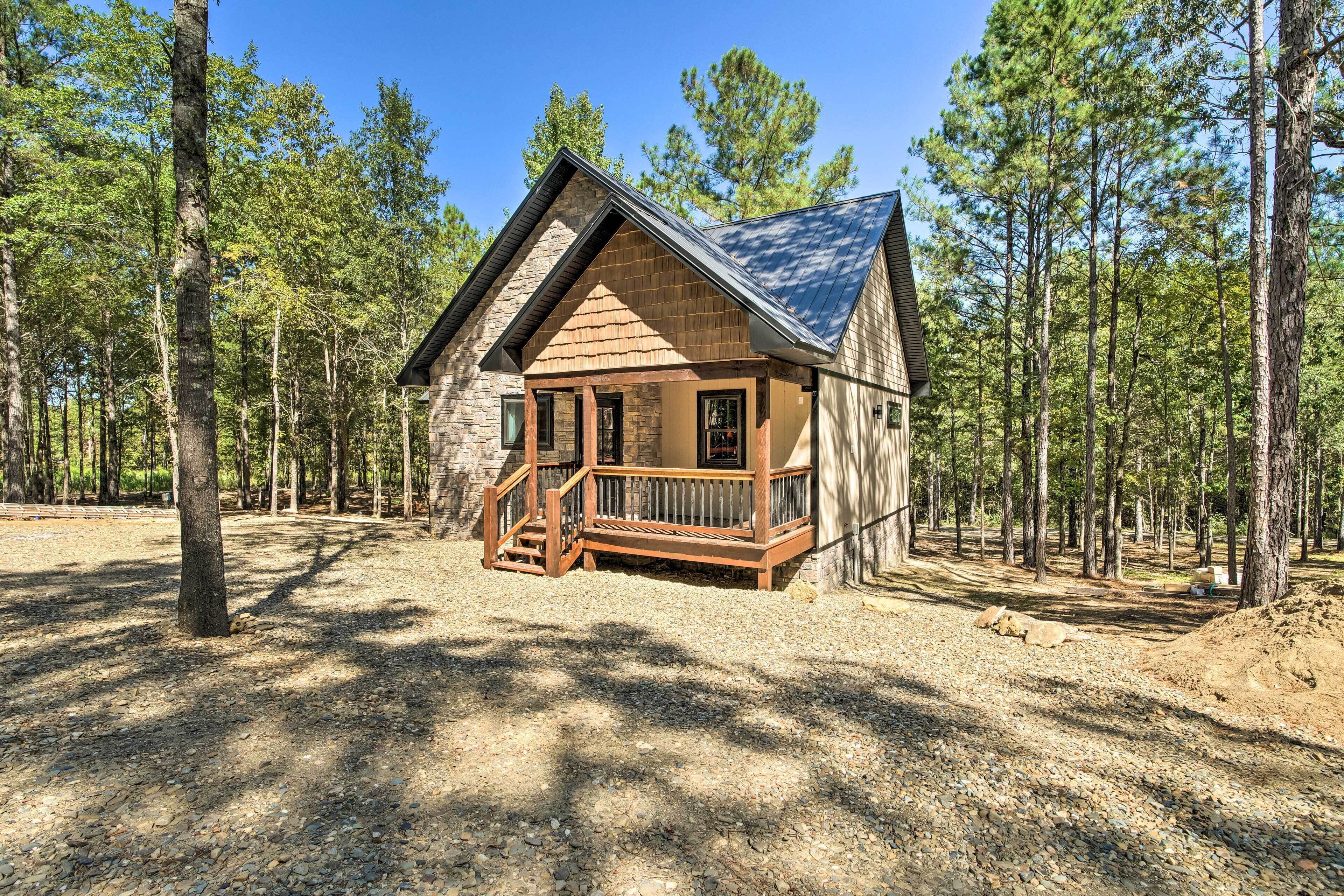 Una cabaña con terraza de madera y base de piedra, rodeada de bosque.