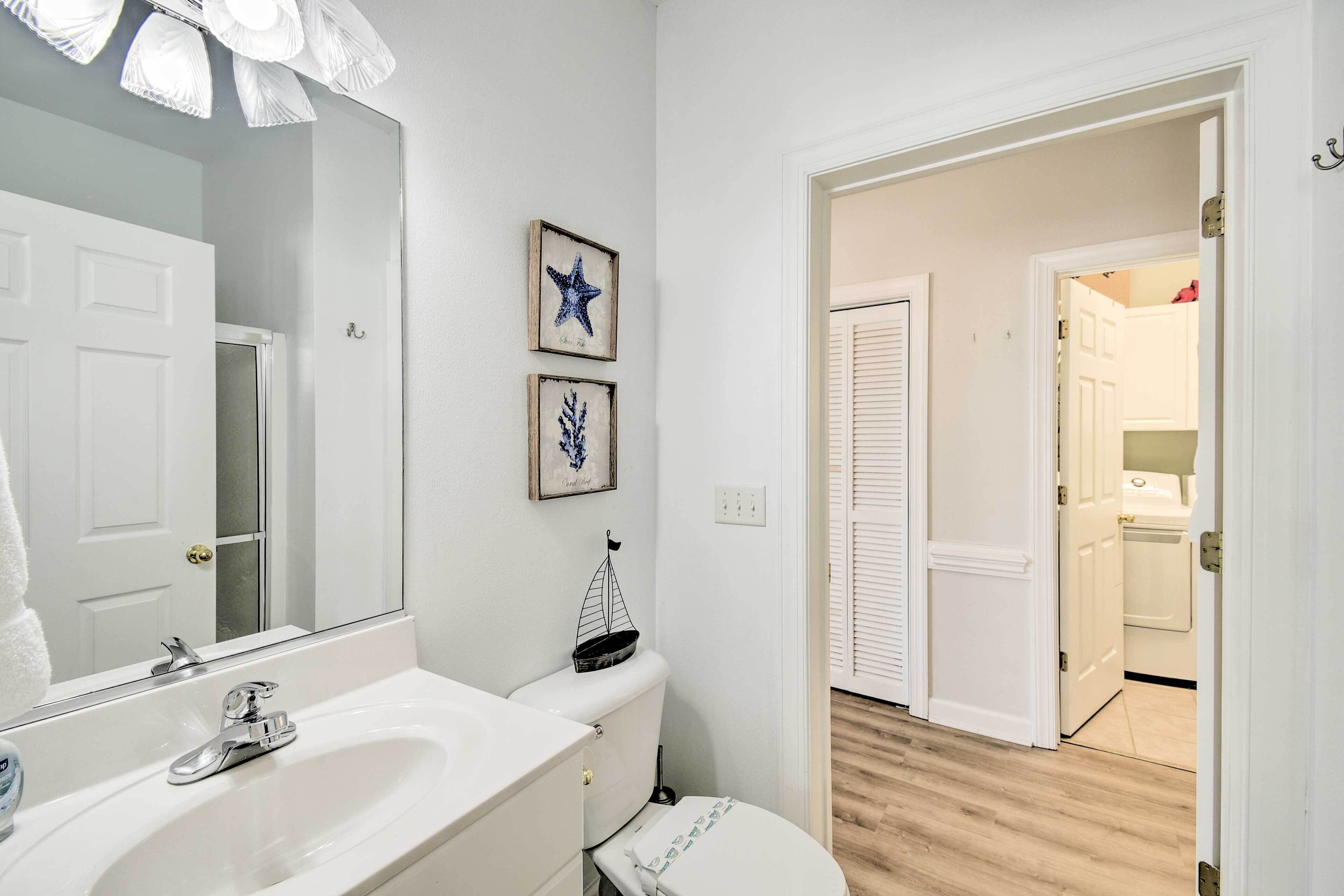 A bathroom with a white sink, a mirror, and a toilet. There are two framed pictures on the wall.