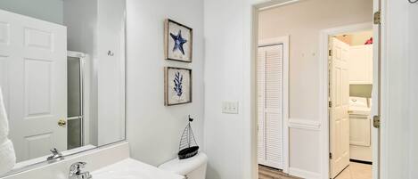 A bathroom with a white sink, a mirror, and a toilet. There are two framed pictures on the wall.