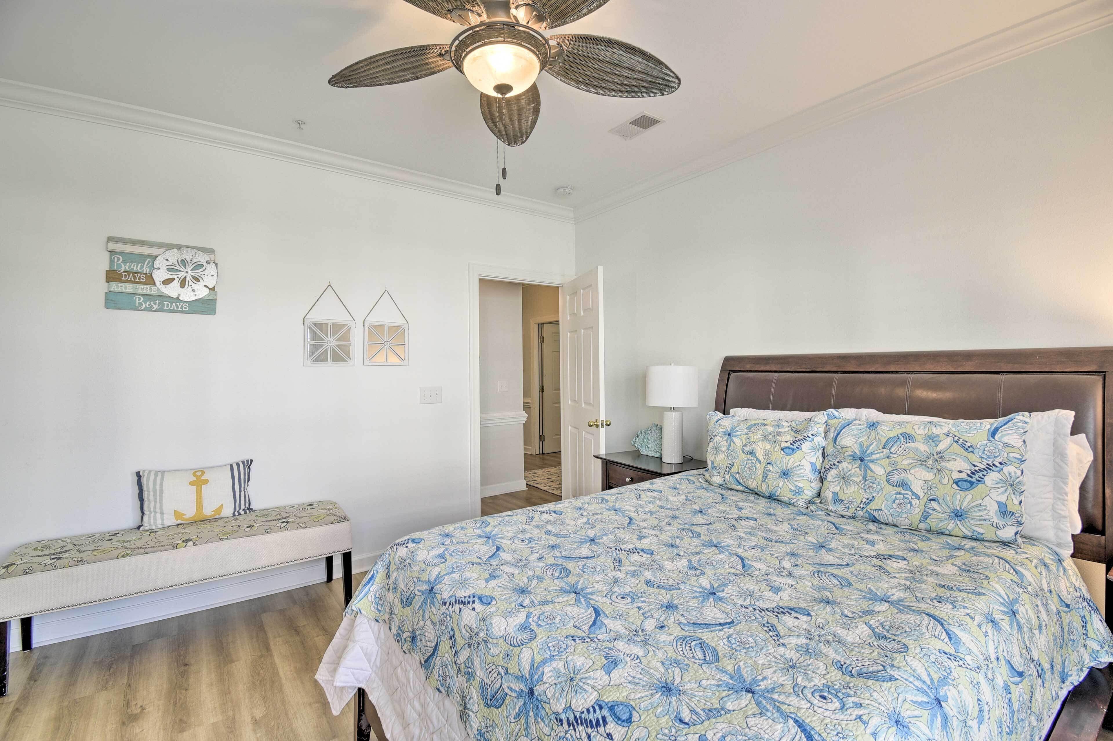 Ein Schlafzimmer mit einem großen Bett, einer Bank, einem Deckenventilator und einer Tür zu einem anderen Raum.