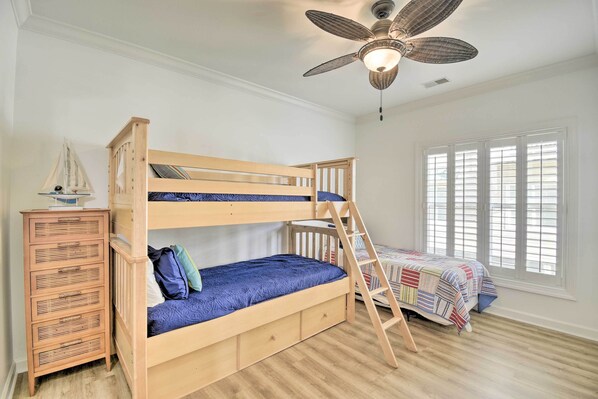 A bunk bed with a ladder, a dresser, and a ceiling fan in a room with wooden flooring and a window with blinds. - Ocean Isle Condo With Community Pool & Hot Tub! (Ocean Isle Beach)