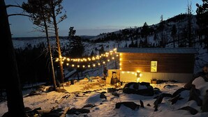 A wooden cabin with a snow-covered yard, string lights, and a chair outside.