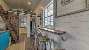 A kitchen with a wooden staircase, a bar area with stools, and a large window with a view.