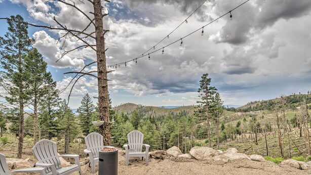 An outdoor seating area with Adirondack chairs, a fire pit, and a view of a mountainous landscape.