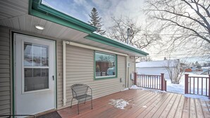 A wooden deck with a metal chair, a door with a window, and a snow-covered ground.