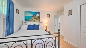 Une chambre à coucher avec un lit, un tableau représentant une ville côtière, une lampe de chevet et une vue sur un couloir.