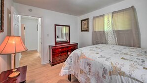 Une chambre à coucher comprenant un lit, une commode, un miroir, une lampe et une porte donnant sur une autre pièce.