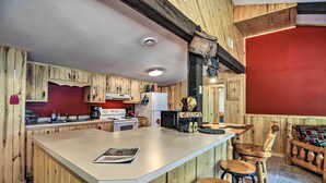 A kitchen with wooden cabinets, a central island, and a red accent wall. - Rustic Mcgregor Retreat on Big Sandy Lake! (McGregor)