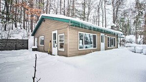 A cabin with a green roof, surrounded by snow-covered ground and trees. - Rustic Mcgregor Retreat on Big Sandy Lake! (McGregor)