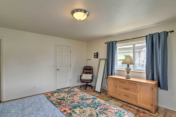A bedroom with a bed, a dresser, a chair, a mirror, and a window with curtains.
