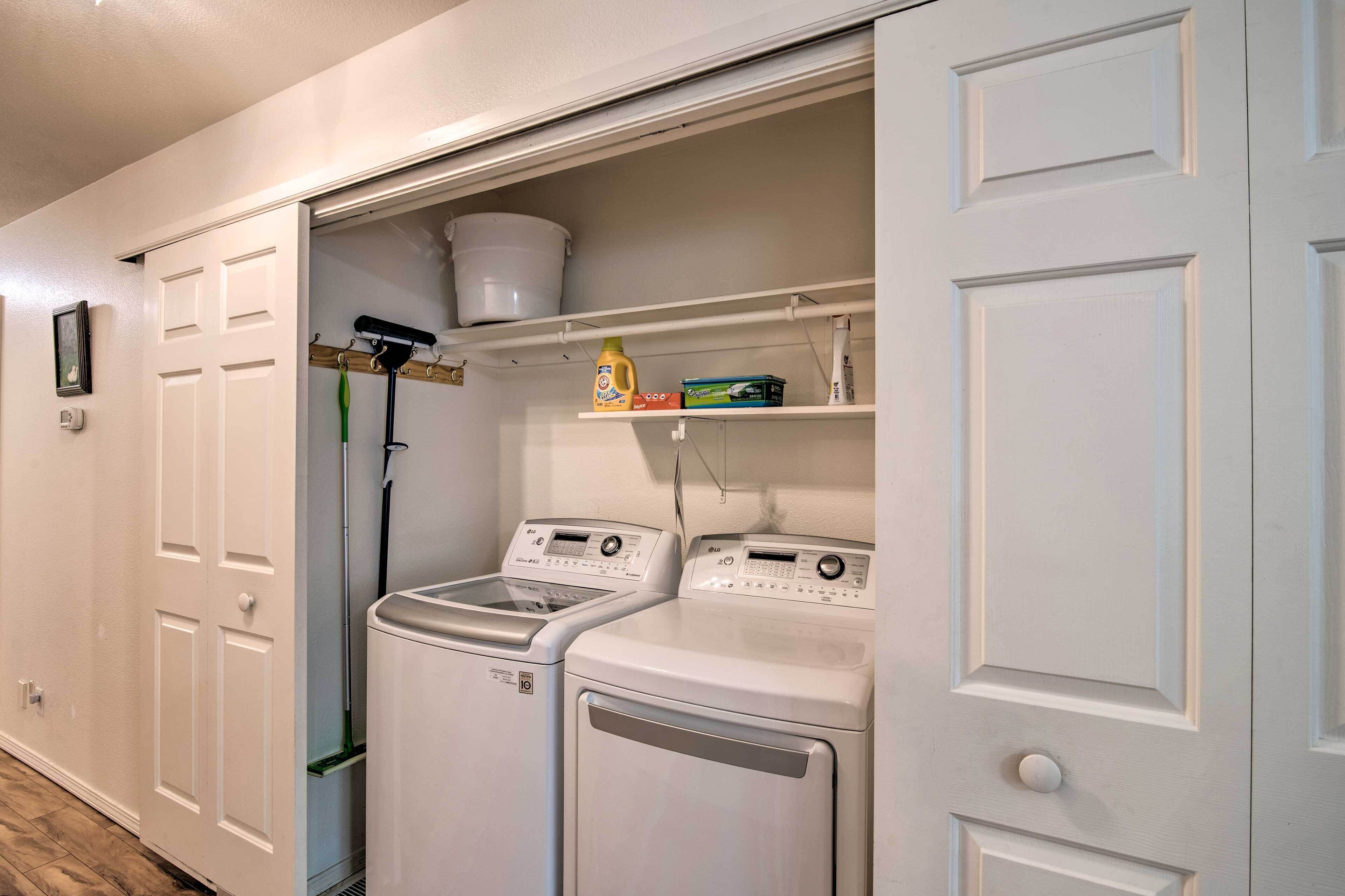 A laundry room with two front-loading washing machines, a drying rack, and a shelf with laundry supplies.