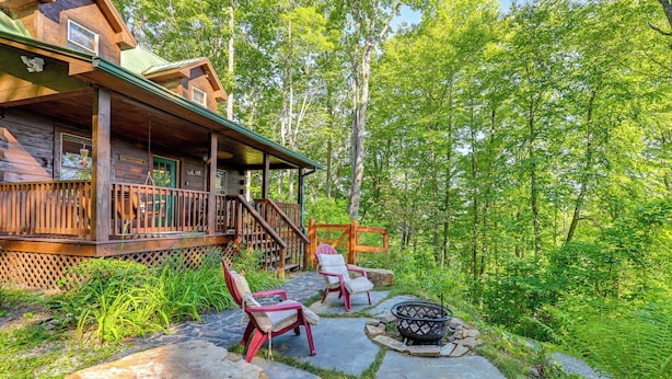A cabin with a porch, two Adirondack chairs, a fire pit, and a stone pathway surrounded by greenery. - Near Hikes & River! Pet-friendly Bryson City Haven (Bryson City)