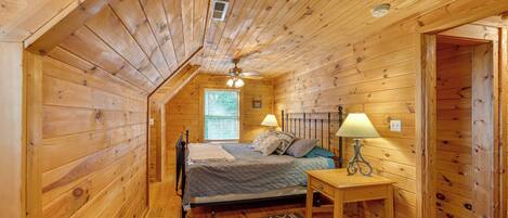 A wooden cabin bedroom with a bed, bedside table, lamp, and a window with blinds.