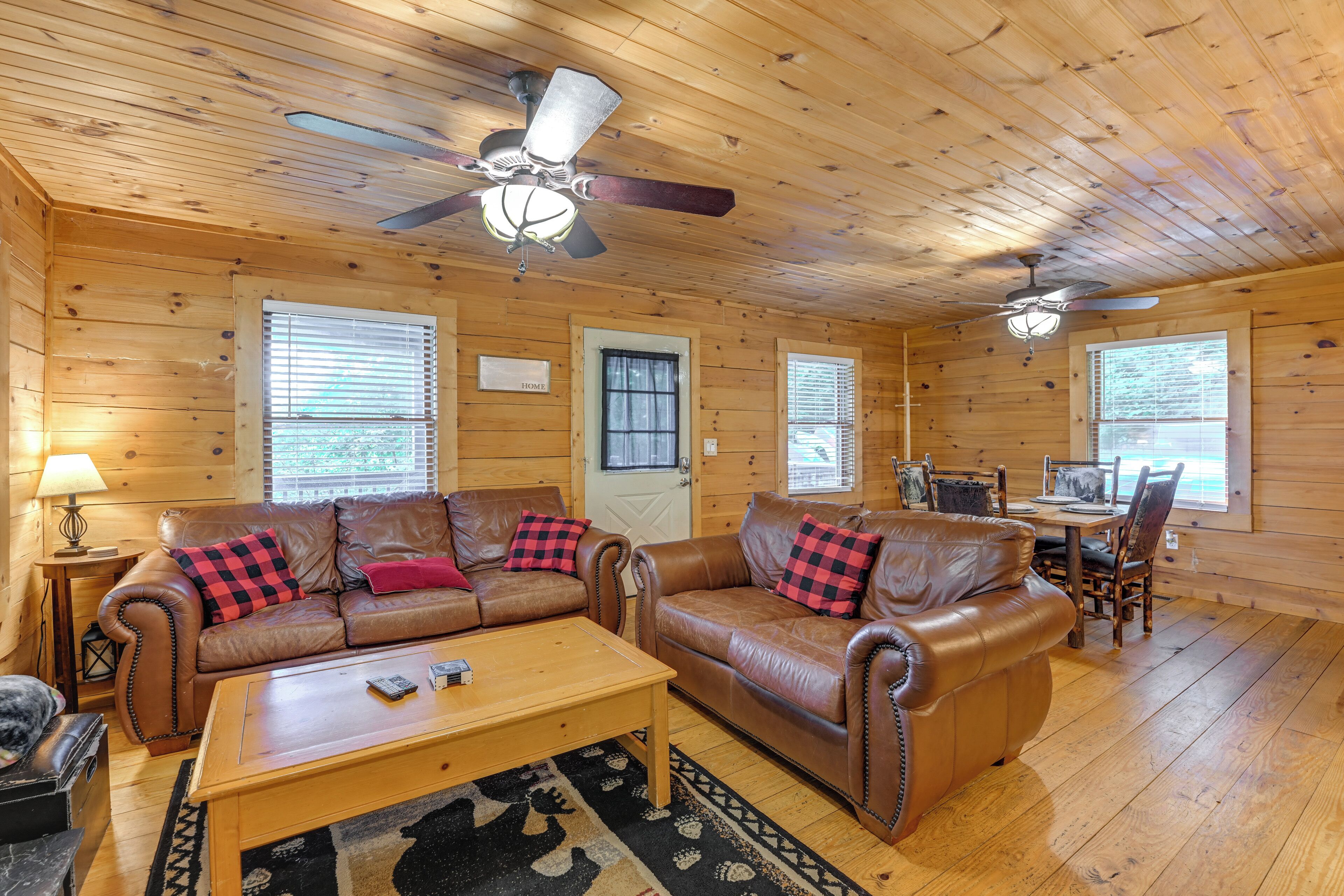 A wooden cabin interior with two leather sofas, a wooden coffee table, and a dining table with chairs.