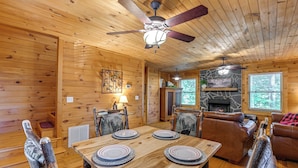 A wooden cabin interior with a dining table set for four, a fireplace, and a stone accent wall. - Near Hikes & River! Pet-friendly Bryson City Haven (Bryson City)