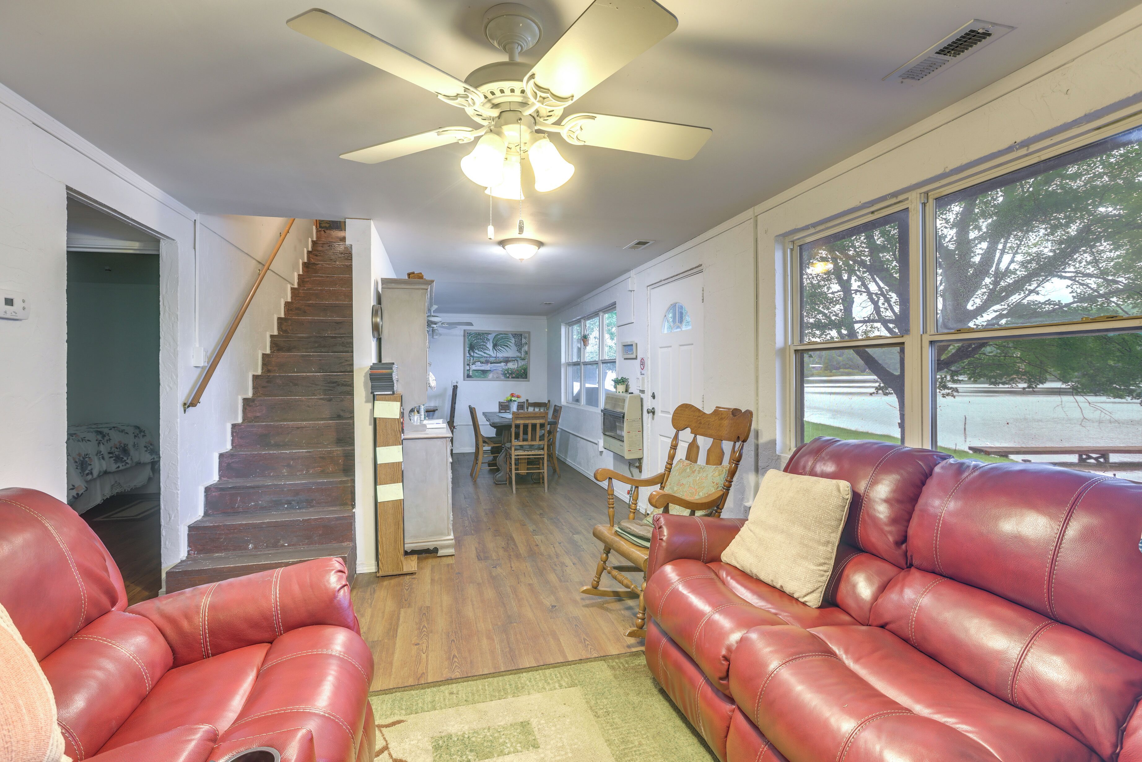 A spacious living room with a red leather couch, a wooden rocking chair, and a staircase leading to another level.