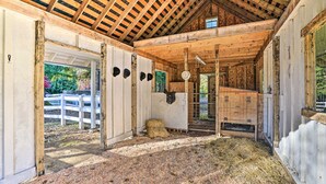 A barn interior with wooden beams, hay on the floor, and a white fence outside. - Roomy Group Getaway in Snohomish (Snohomish)