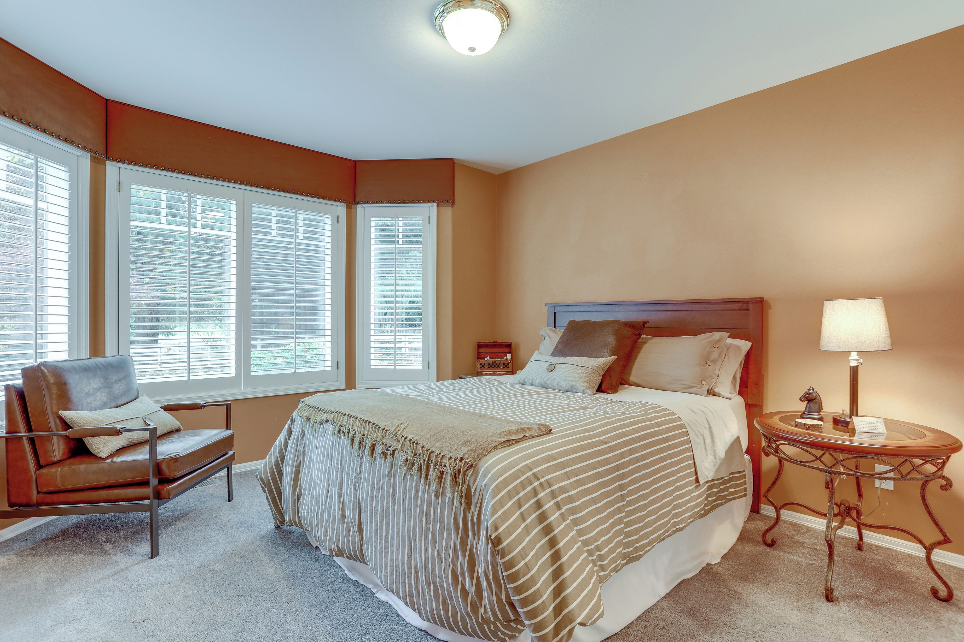 A bedroom with a large bed, a chair, a nightstand, and a lamp.