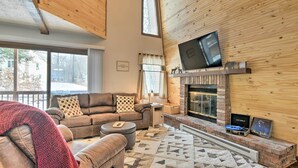 Una sala de estar acogedora con chimenea, un televisor montado encima y un amplio ventanal con vistas al exterior.