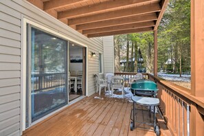 A wooden deck with a covered area, a sliding glass door, outdoor chairs, and a grill.