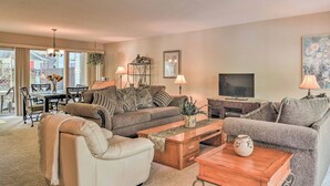 A living room with a sofa, armchairs, a coffee table, a TV, and a dining area with a table and chairs. - Lakefront Townhome w/ View in Hot Springs Village! (Hot Springs Village)