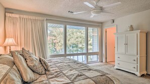 A bedroom with a large bed, a ceiling fan, a dresser, and a window with a view of trees. - Lakefront Townhome w/ View in Hot Springs Village! (Hot Springs Village)
