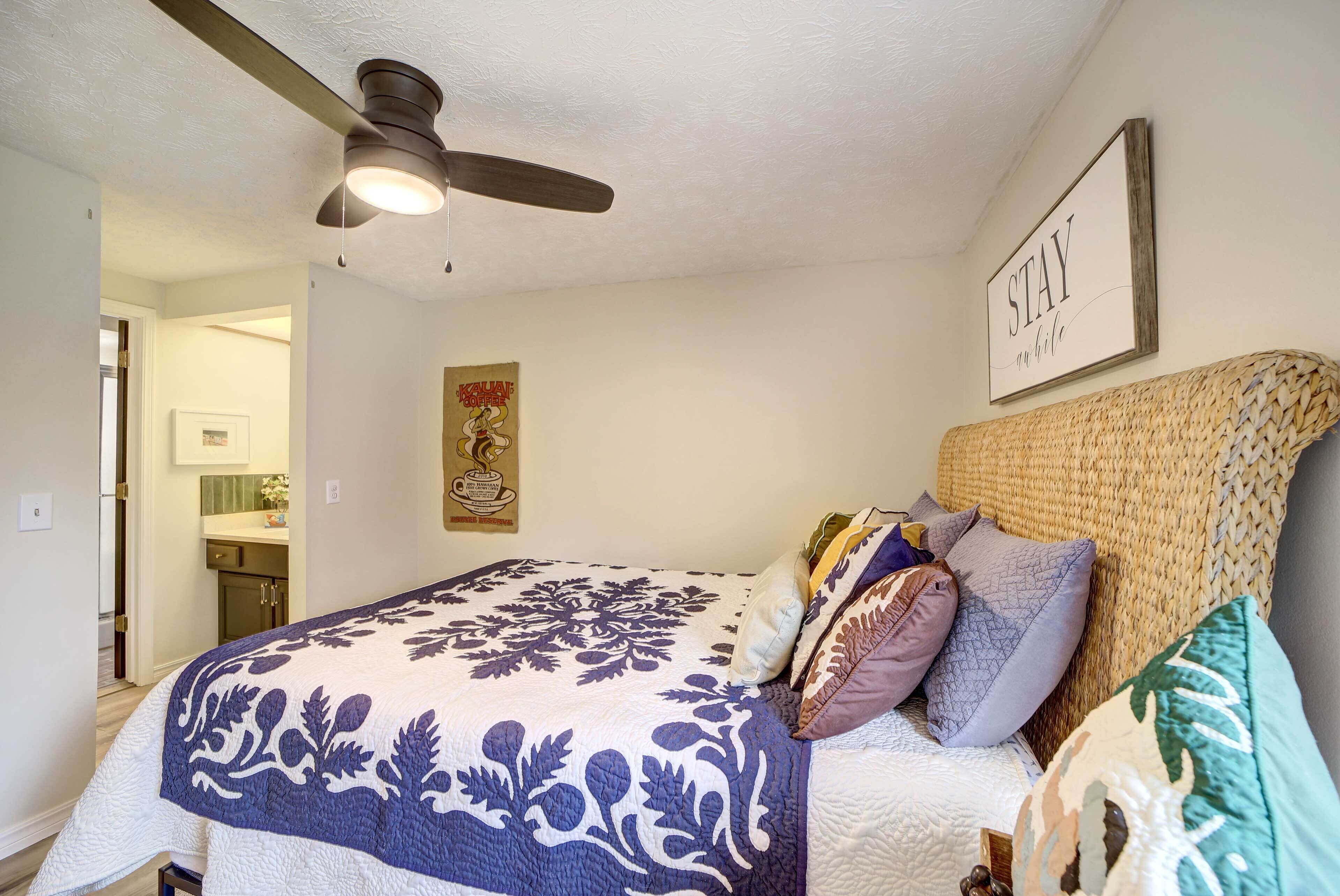 A bedroom with a bed, a ceiling fan, a wall-mounted sign, and a framed picture.