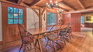 A wooden dining room with a large table and chairs, a chandelier, and a view through the windows. - 10 Mi to Hot Springs Natl Park: Home w/ Grill! (Hot Springs)