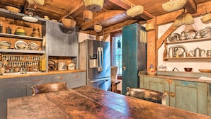 A rustic kitchen with wooden beams, a large wooden table, and shelves with kitchenware. - 10 Mi to Hot Springs Natl Park: Home w/ Grill! (Hot Springs)