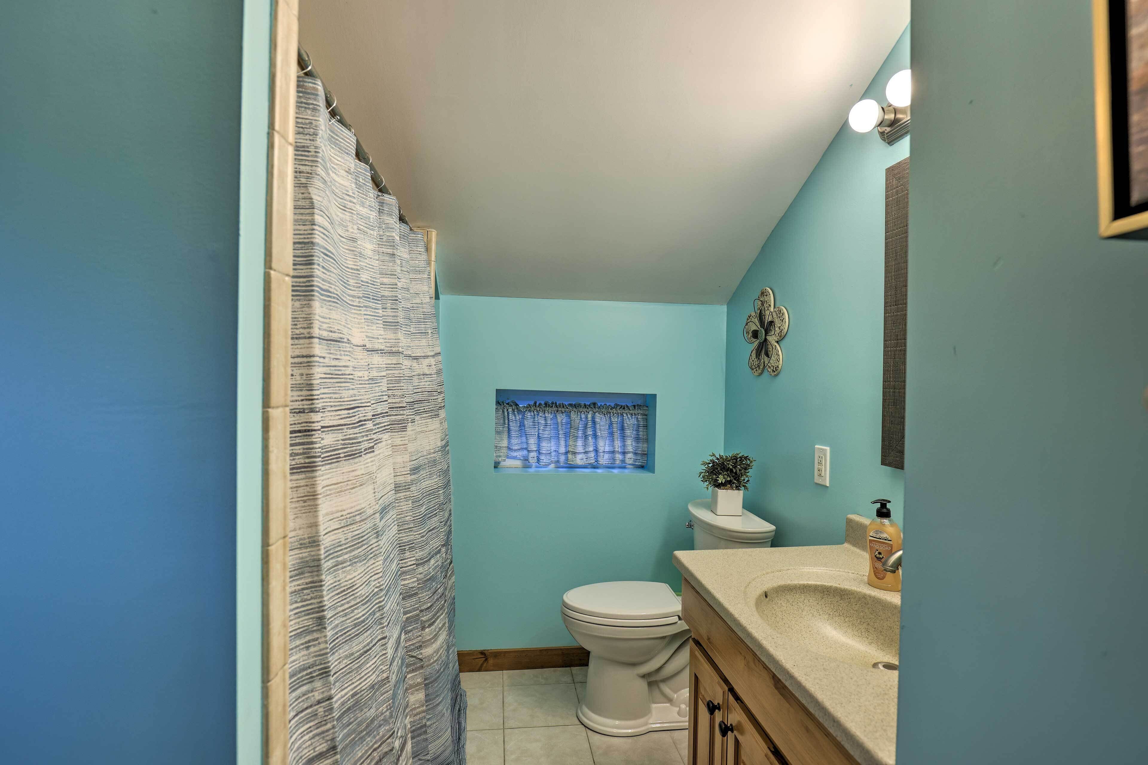 A bathroom with a shower curtain, a toilet, a sink, and a small window with a view of trees.