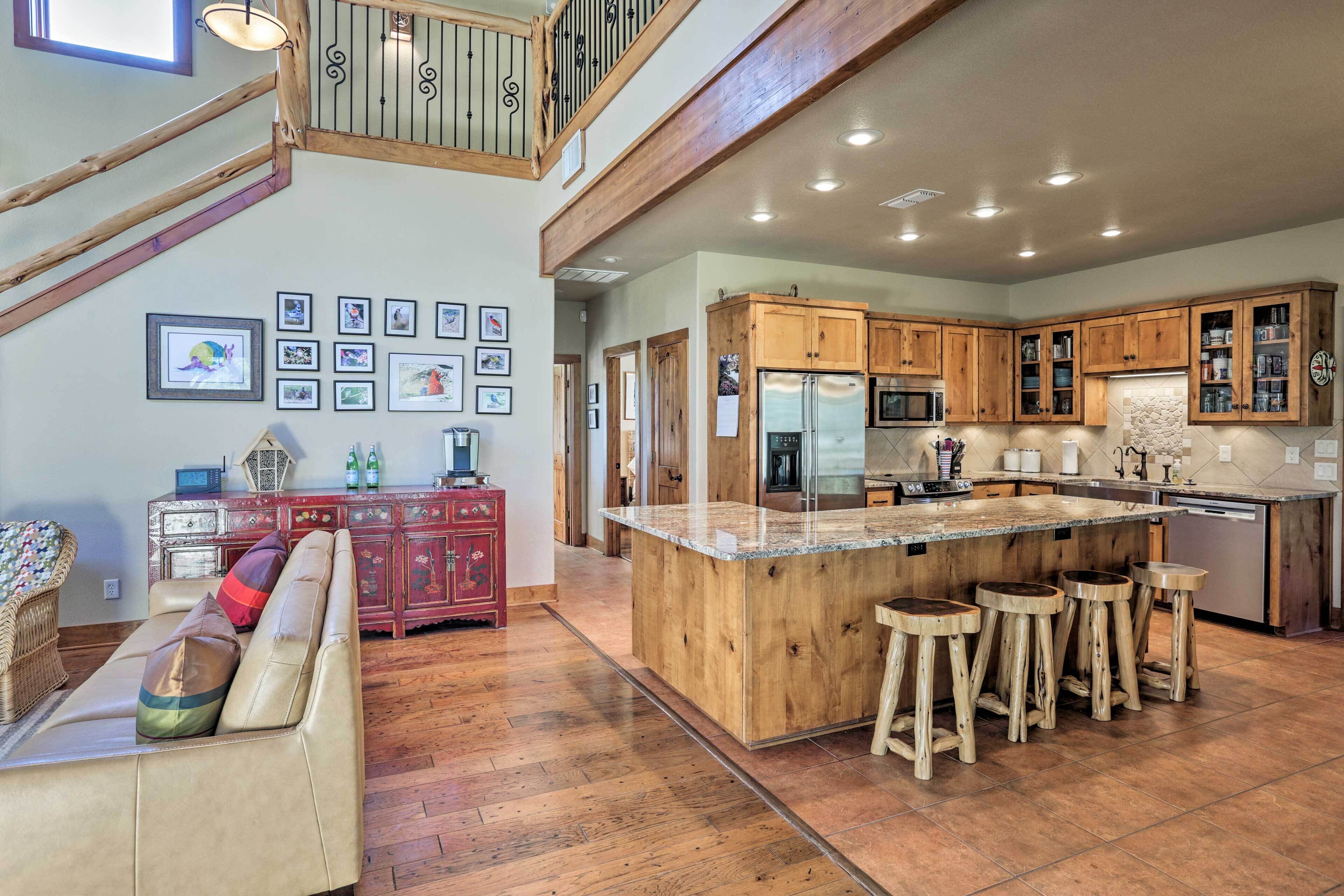 A spacious kitchen with wooden cabinets, a large island with stools, and a dining area with a sofa and a red cabinet.